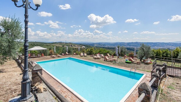 A rectangular swimming pool with a clear blue water surface, surrounded by a stone wall and a wooden deck. - Belvilla by OYO Istrice (Capraia E Limite (fi))