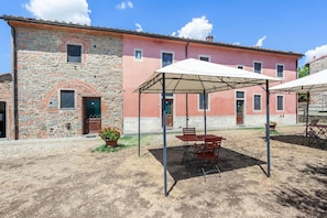A rustic building with a stone facade and a pink-painted upper section. There is a covered outdoor seating area with tables and chairs. - Belvilla by OYO Istrice (Capraia E Limite (fi))