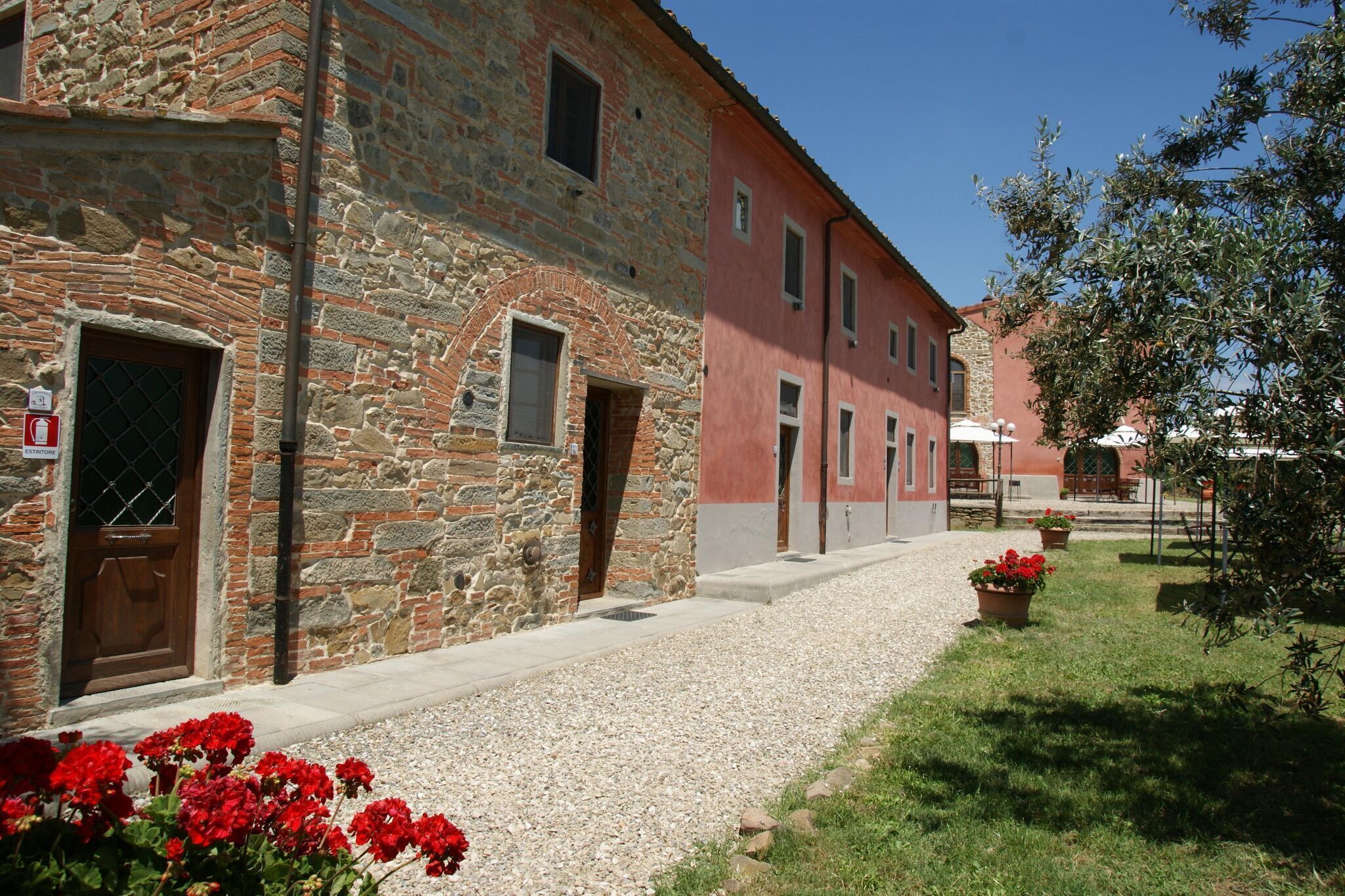 Un edificio in pietra con una facciata rossa, un vialetto sterrato e vasi di piante.