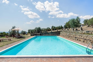 A rectangular swimming pool with a stone wall and a clear blue sky. - Belvilla by OYO Istrice (Capraia E Limite (fi))