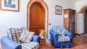 A room with two blue armchairs, a wooden door with an arch, and a small table with a flower vase. - Belvilla by OYO Istrice (Capraia E Limite (fi))