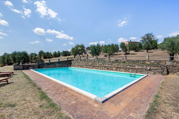 A rectangular swimming pool with a stone wall and a stone pathway leading to it.