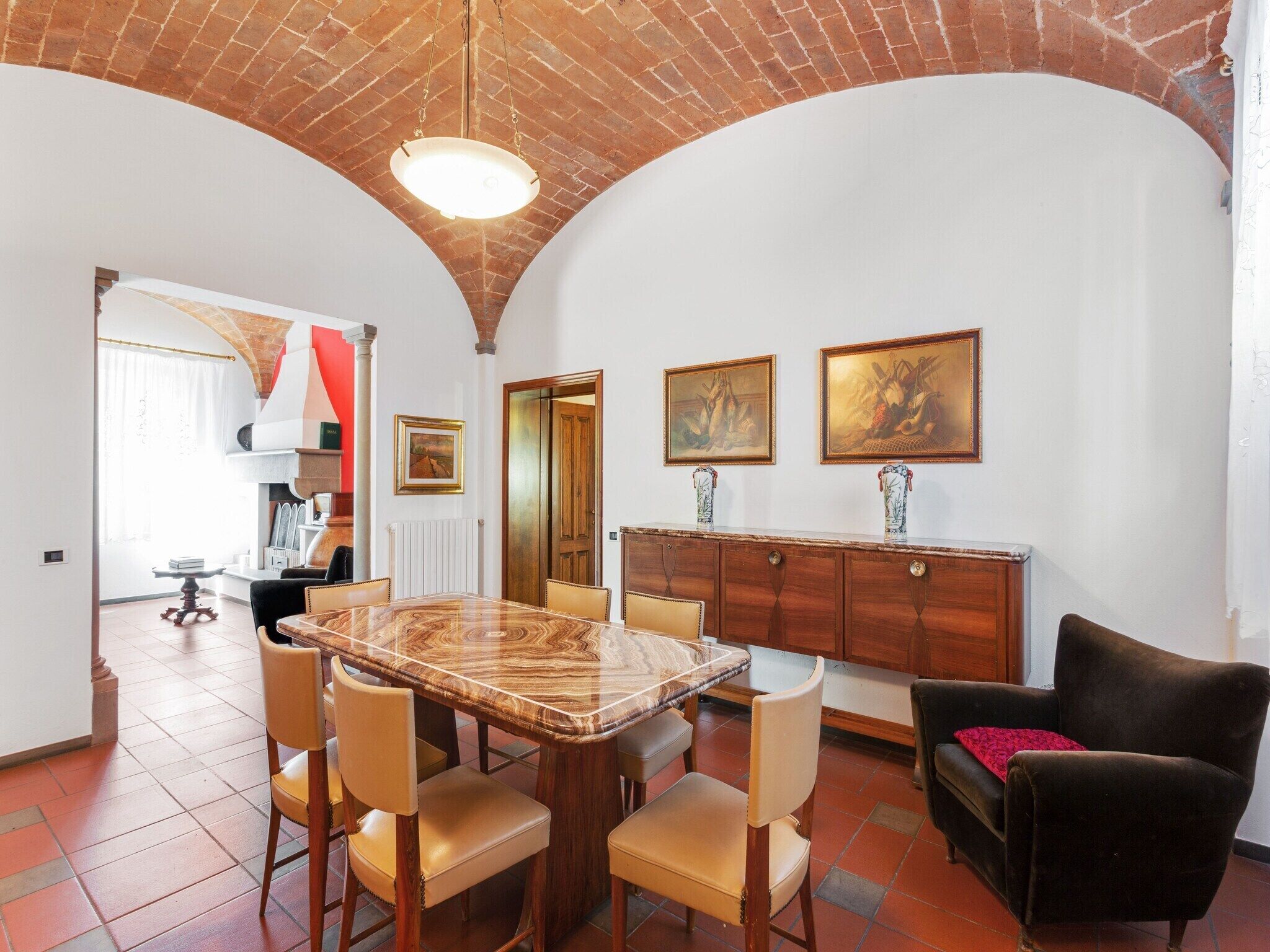 Un coin repas avec une table en marbre, des chaises en bois, un canapé noir et un meuble contenant des tableaux.