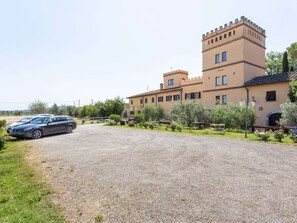 Un grand bâtiment doté d’une tour, d’une allée gravillonnée et de voitures garées.
