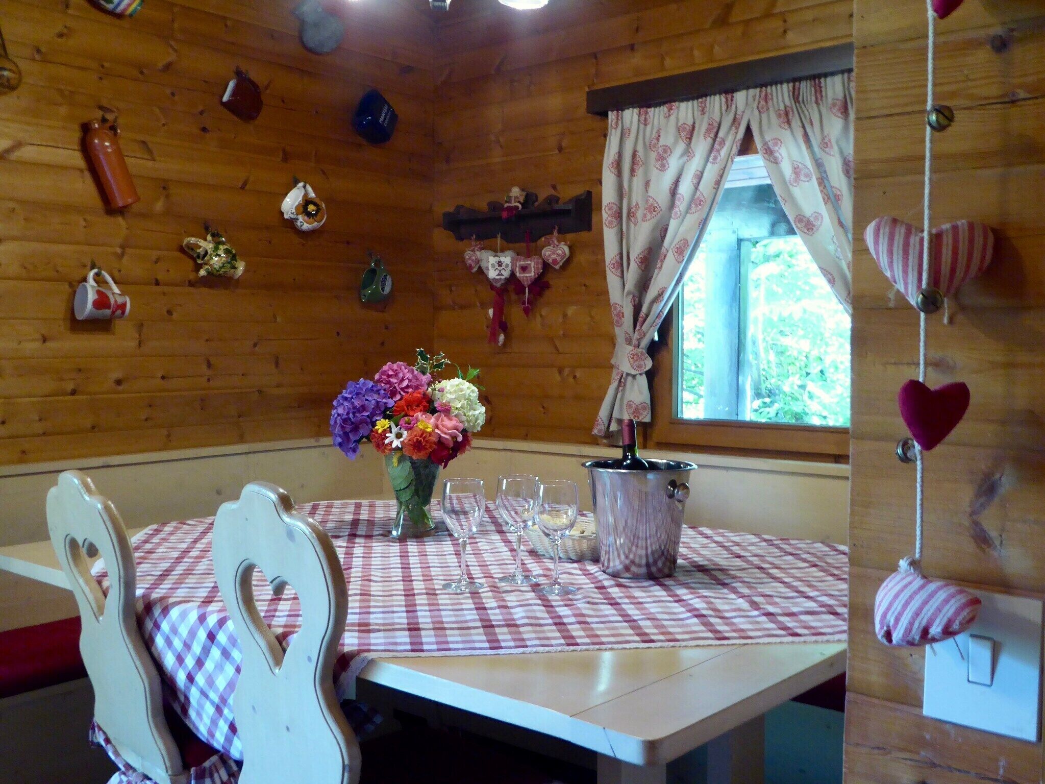 Ein Interieur einer Holzhütte mit einem Esstisch für zwei Personen, einer Blumenvase und einer Weinflasche.