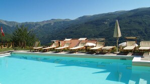 A pool with lounge chairs and a flag, surrounded by mountains. - Alpine Getaway in Tuscany (Cutigliano)