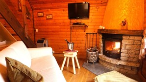 A cozy cabin interior with a stone fireplace, a white sofa, and a television mounted on the wall. - Alpine Getaway in Tuscany (Cutigliano)