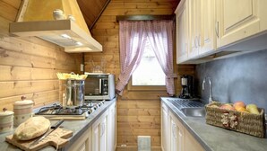 A compact kitchen with wooden walls, a gas stove, a microwave, and a sink. - Alpine Getaway in Tuscany (Cutigliano)