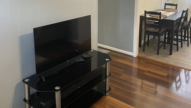 A modern living room with a flat-screen TV, a black entertainment unit, and a 'Welcome to our home' sign. - Cozy 3 bedroom house (South Glens Falls)