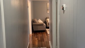 A hallway with a patterned rug, wooden flooring, and a beige sofa in the background. - Cozy 3 bedroom house (South Glens Falls)