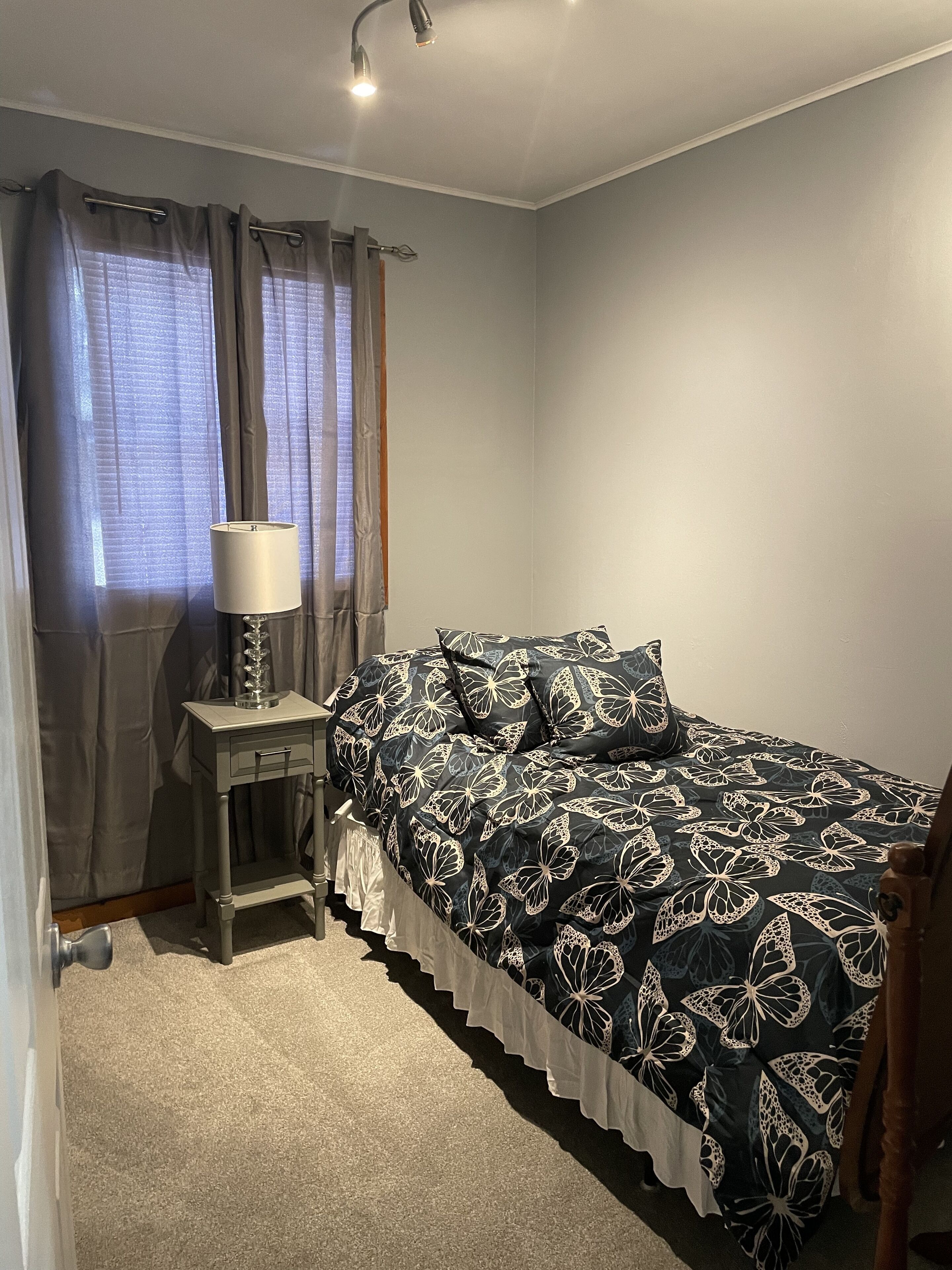 Un dormitorio con cama, una mesita de noche con lámpara y una ventana con cortinas.