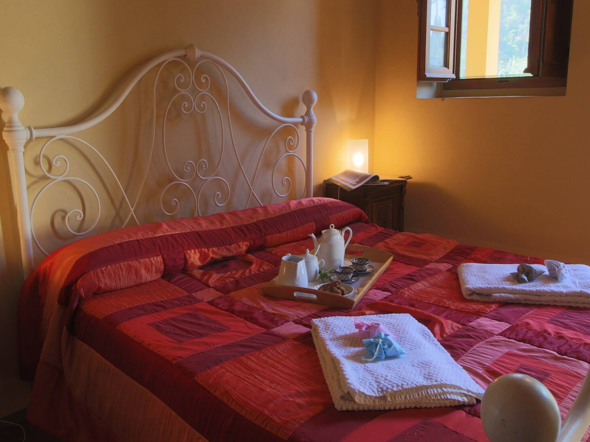 Een netjes opgemaakt bed met een rode quilt, een dienblad met theeservies en handdoeken op het bed.