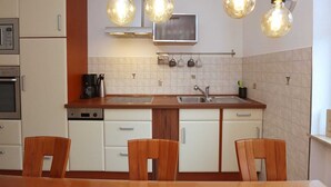 A compact kitchen with a central island, white cabinetry, and a microwave. There are three hanging light bulbs above the island, and a small television mounted on the wall.