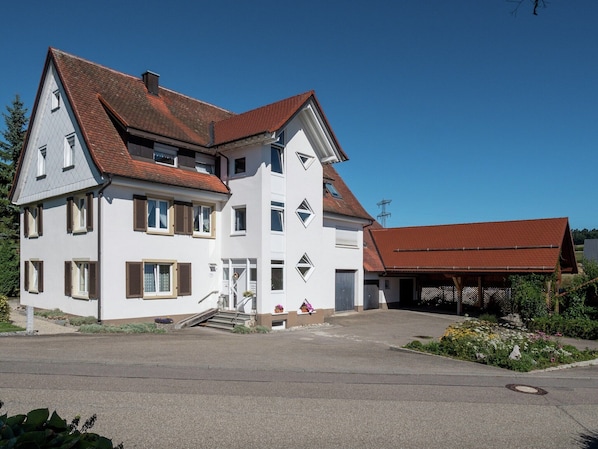 Une maison à deux étages avec un toit recouvert de tuiles rouges, une véranda et un petit jardin.