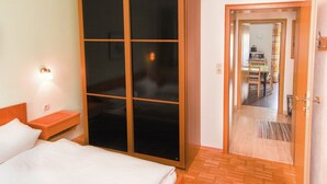 Quarto de hotel com um guarda-roupa espaçoso, uma cama com lençóis brancos, uma mesa de cabeceira e uma luminária na parede.