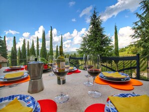 Zona de comedor al aire libre con una vista panorámica, mostrando una mesa servida con platos, vasos y una botella de vino.