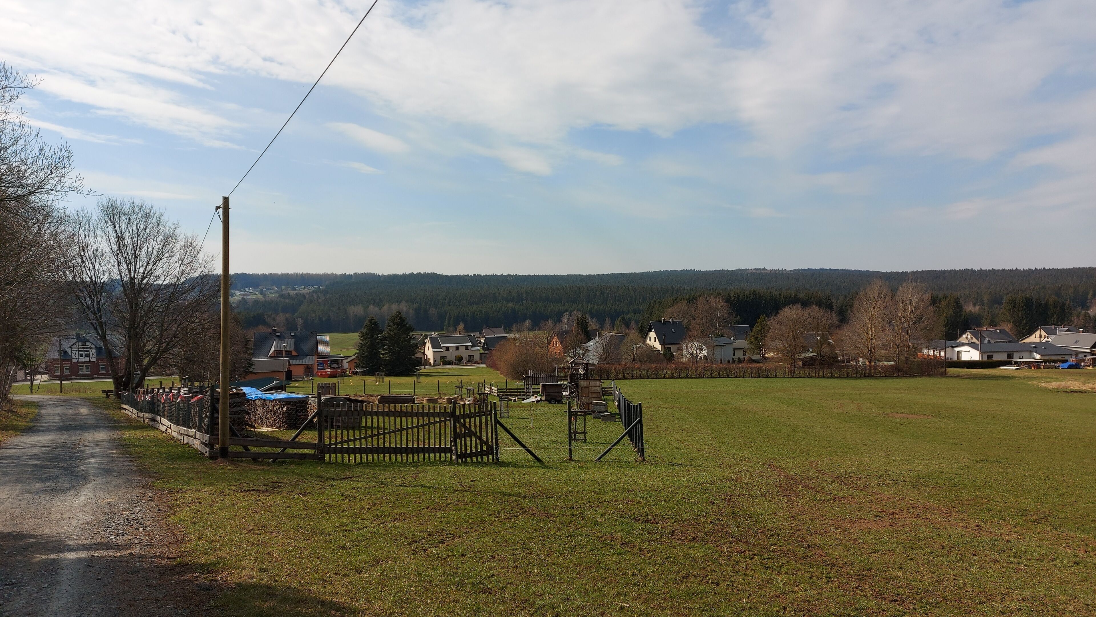A rural landscape with a fenced area, a road, and houses in the background.