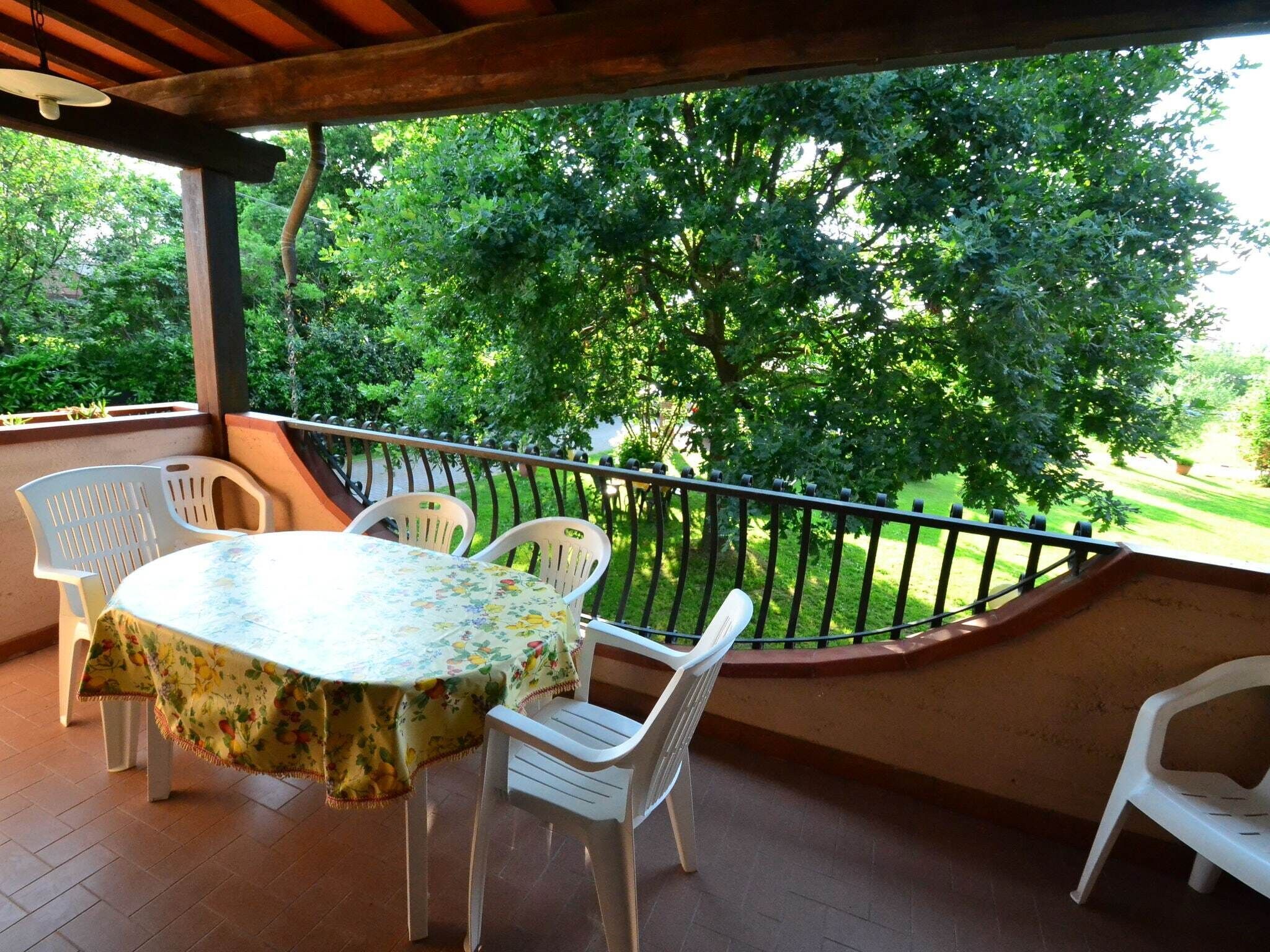 Een overdekt terras met een ronde tafel en vier stoelen, omgeven door een zwarte metalen balustrade.