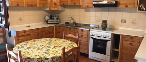 A kitchen with wooden cabinets, a stove, a sink, and a table with a floral tablecloth.