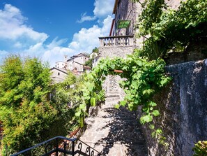 Eine Steintreppe führt zu einem Gebäude mit einem Balkon, umgeben von Grünpflanzen und blauem Himmel.