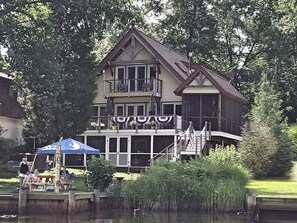 Een groot huis met balkon, een steiger en een klein bootje.