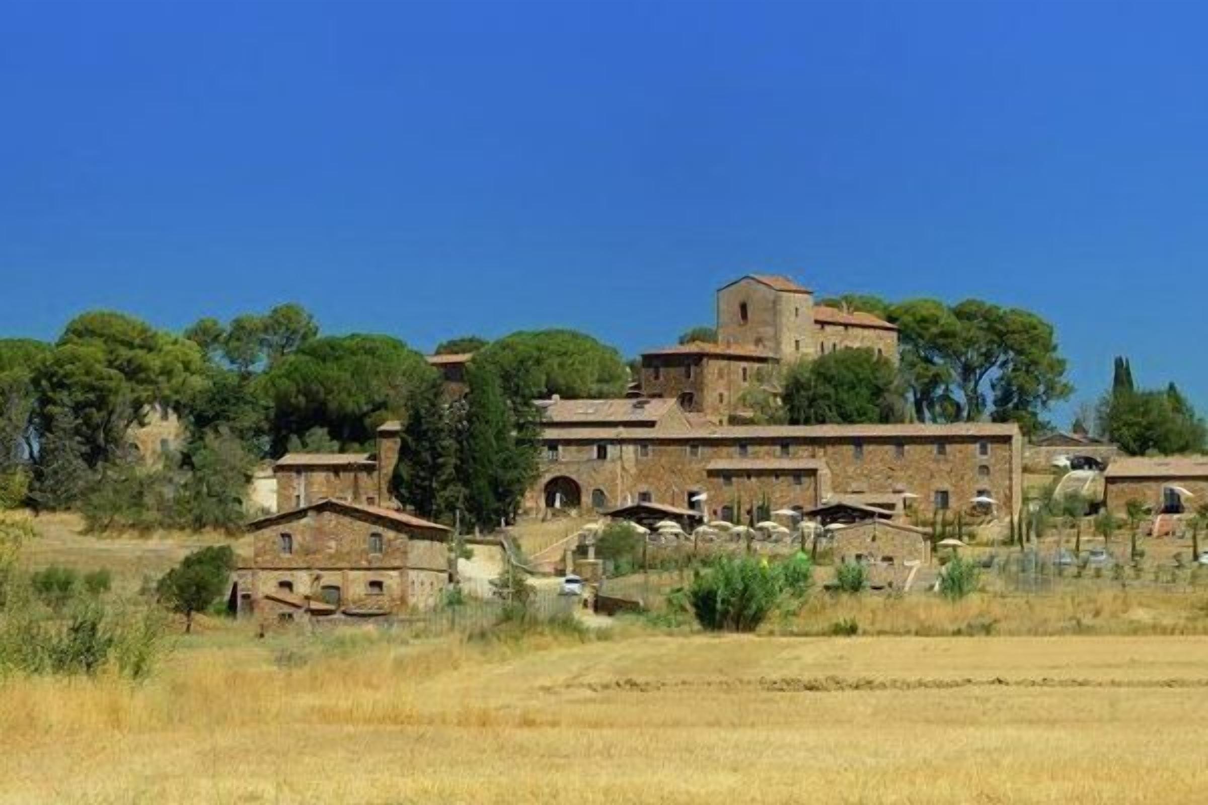 A historic building complex with multiple structures, including a prominent tower, surrounded by fields and trees.