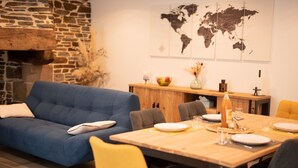 Een moderne woonkamer met een blauwe bank, gele stoelen, een houten eettafel voor vier personen en een stenen open haard.