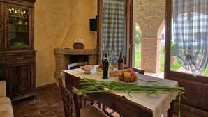 Un comedor rústico con una mesa de madera dispuesta para dos comensales, una chimenea de piedra y vistas a zonas verdes al exterior.