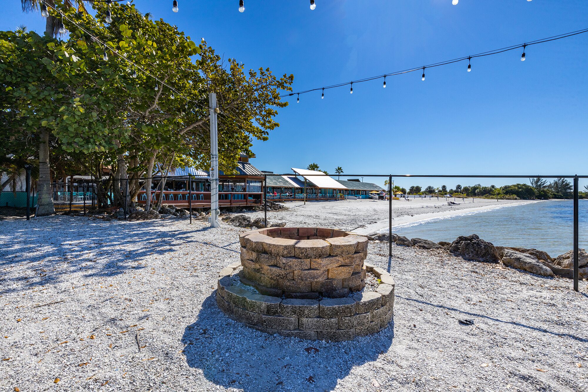 A beachfront property with a stone fire pit, a beach, and a building with a blue roof.