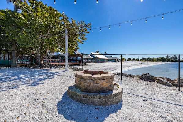 A beachfront property with a stone fire pit, a beach, and a building with a blue roof.