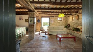 A rustic interior with exposed wooden beams, a stone fireplace, a sofa, and a dining table.