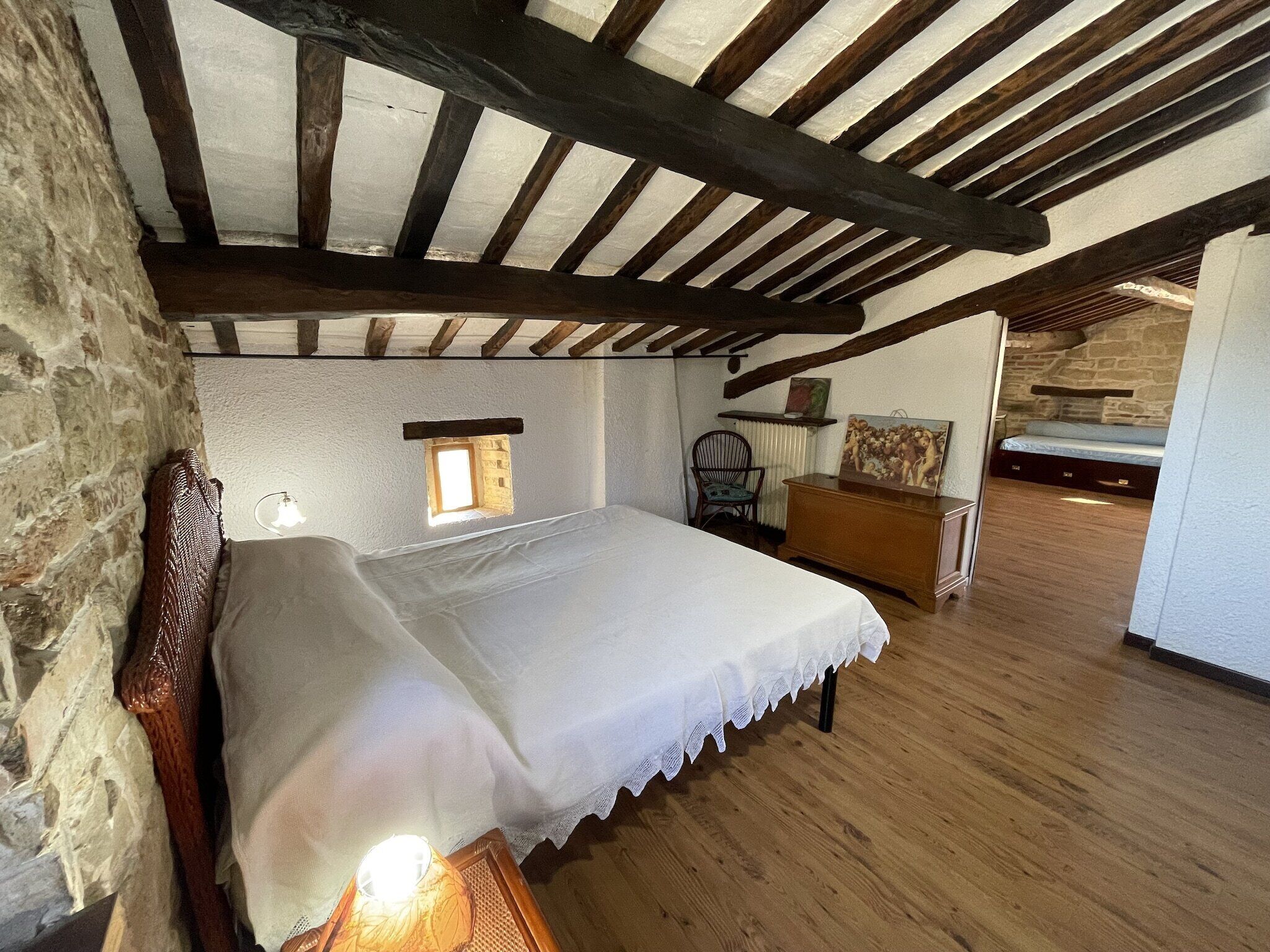 Ein Schlafzimmer mit einem hölzernen Bett, einem kleinen Fenster, einem Stuhl und einer Kommode.