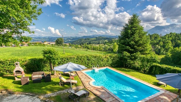 A rectangular swimming pool with a brick border, surrounded by a grassy area with lounge chairs and umbrellas.