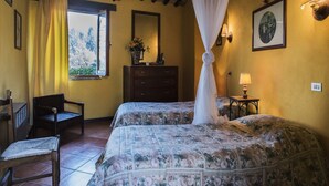 Une chambre avec deux lits, une chaise en bois, une commode, une fenêtre avec des rideaux et une lampe fixée au mur.