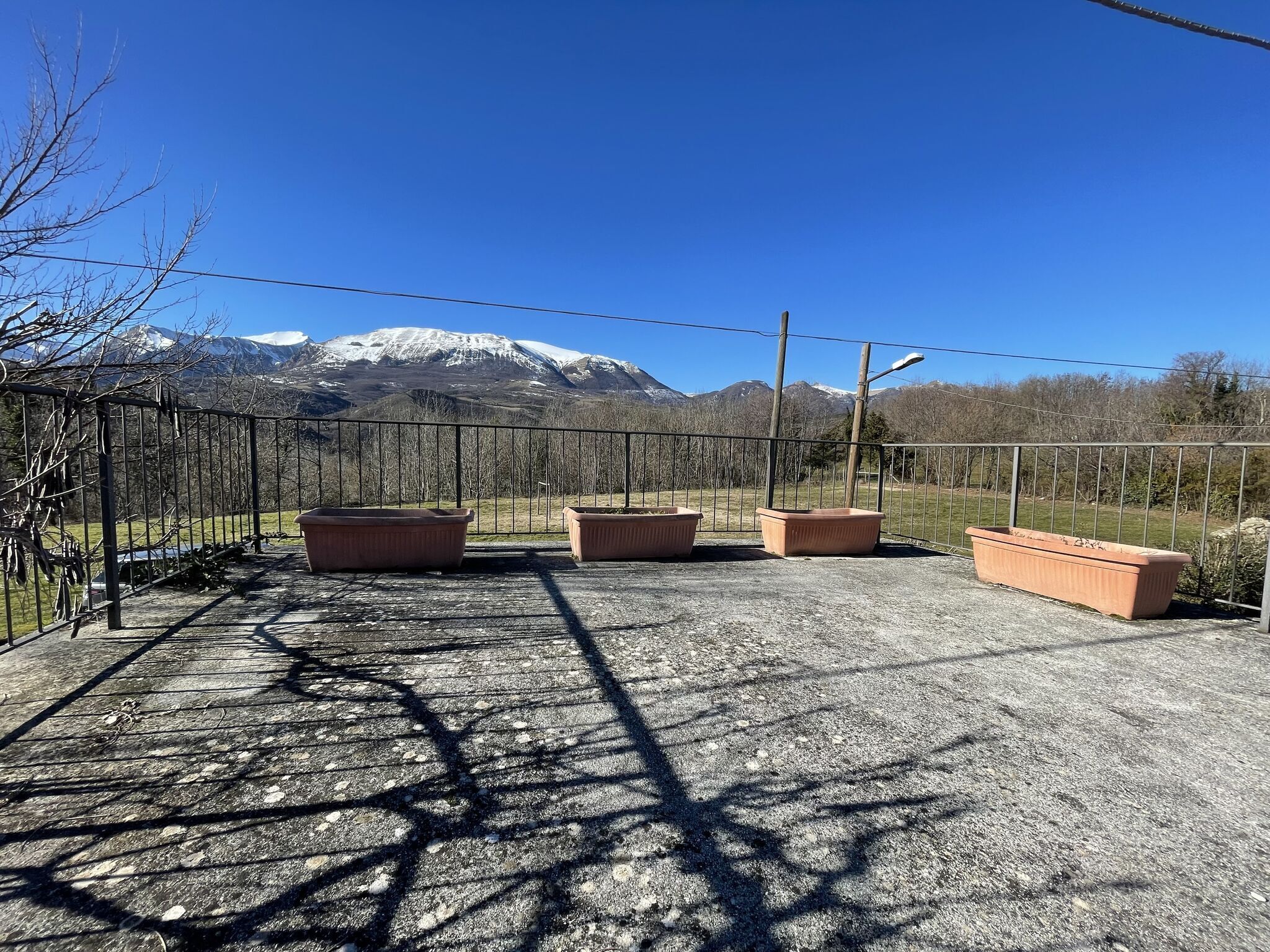 Un balcon agrémenté de jardinières en terre cuite, une clôture en métal et une vue sur des montagnes enneigées.