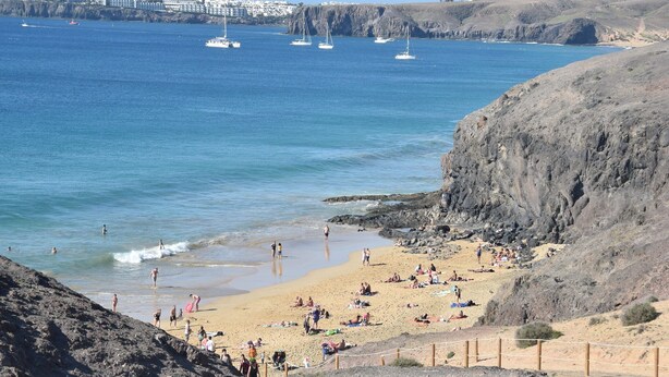 A beach with people sunbathing and swimming, a rocky cliff, and boats in the water. - Terrace Stay Close to Beaches (Playa Blanca)