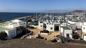 A marina with numerous boats docked, surrounded by white buildings with green accents and a clear view of the sea. - Terrace Stay Close to Beaches (Playa Blanca)