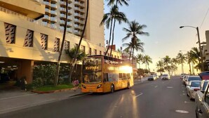 A multi-story hotel with balconies, palm trees, and a bus on the street. - 3 Minute walk to famous Waikiki beach 100% legal with Free Parking  (Honolulu)