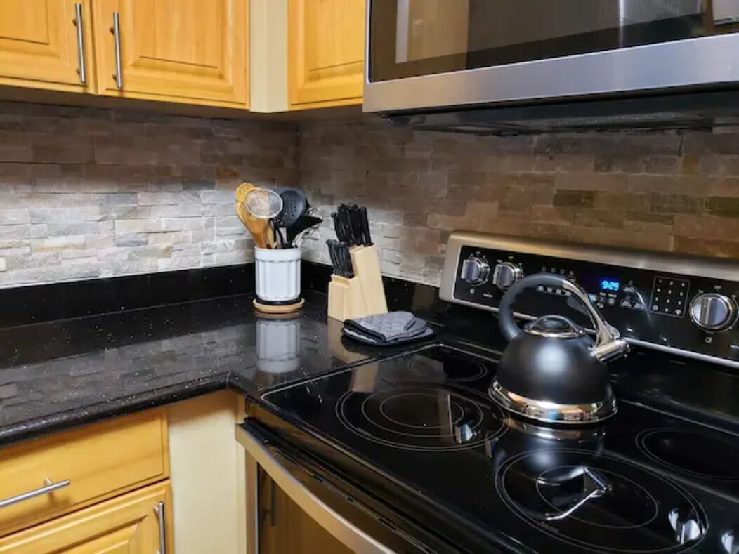 A kitchen with wooden cabinets, a black countertop, a stainless steel stove, and a kettle.