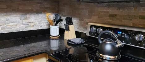 A kitchen with wooden cabinets, a black countertop, a stainless steel stove, and a kettle.
