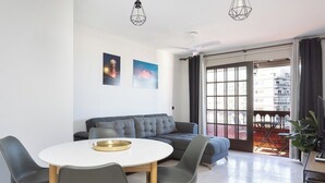 Una sala de estar moderna con una mesa de comedor redonda, un sofá gris y un balcón con vistas a edificios.