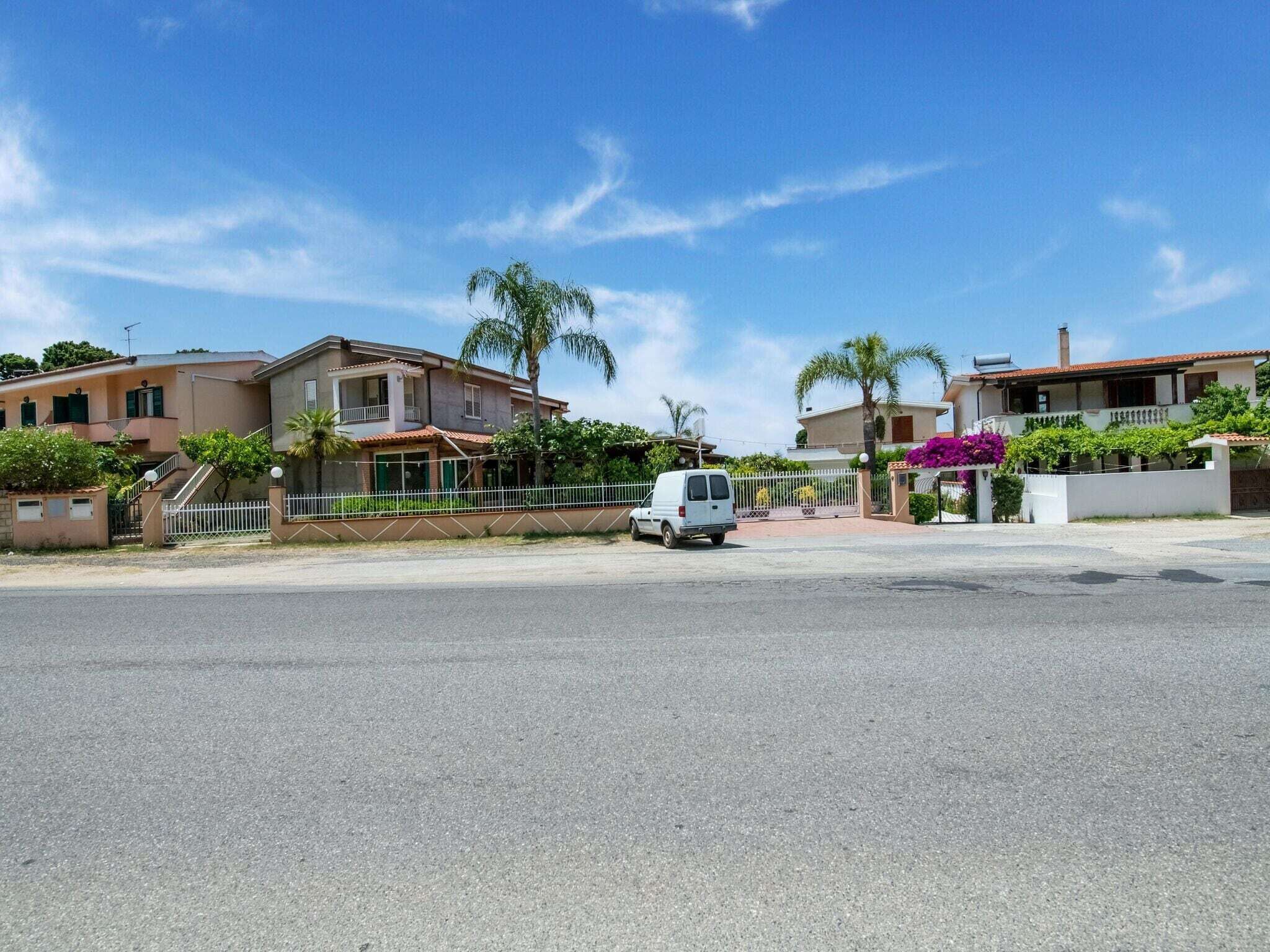 A residential street with houses, a white van parked on the side, and a clear blue sky.