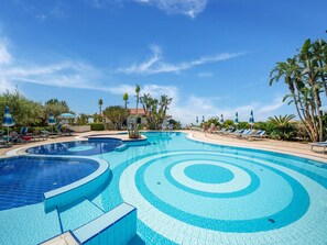 A large, multi-tiered swimming pool with clear blue water, surrounded by lounge chairs and palm trees. - Belvilla by OYO Gattotrilo x 5 (San Nicolò di Ricadi)