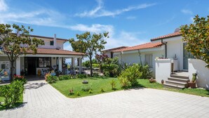 A courtyard with a paved walkway, a covered seating area, and a building with a tiled roof.