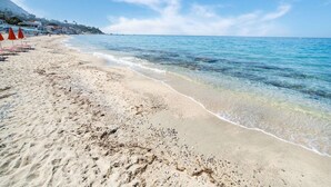 A beach with clear blue water, sandy shore, and red umbrellas.