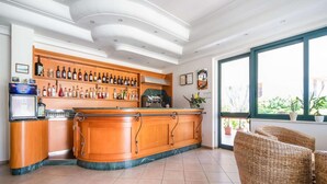 A bar area with a curved wooden counter, shelves with bottles, a refrigerator, and a wicker chair.