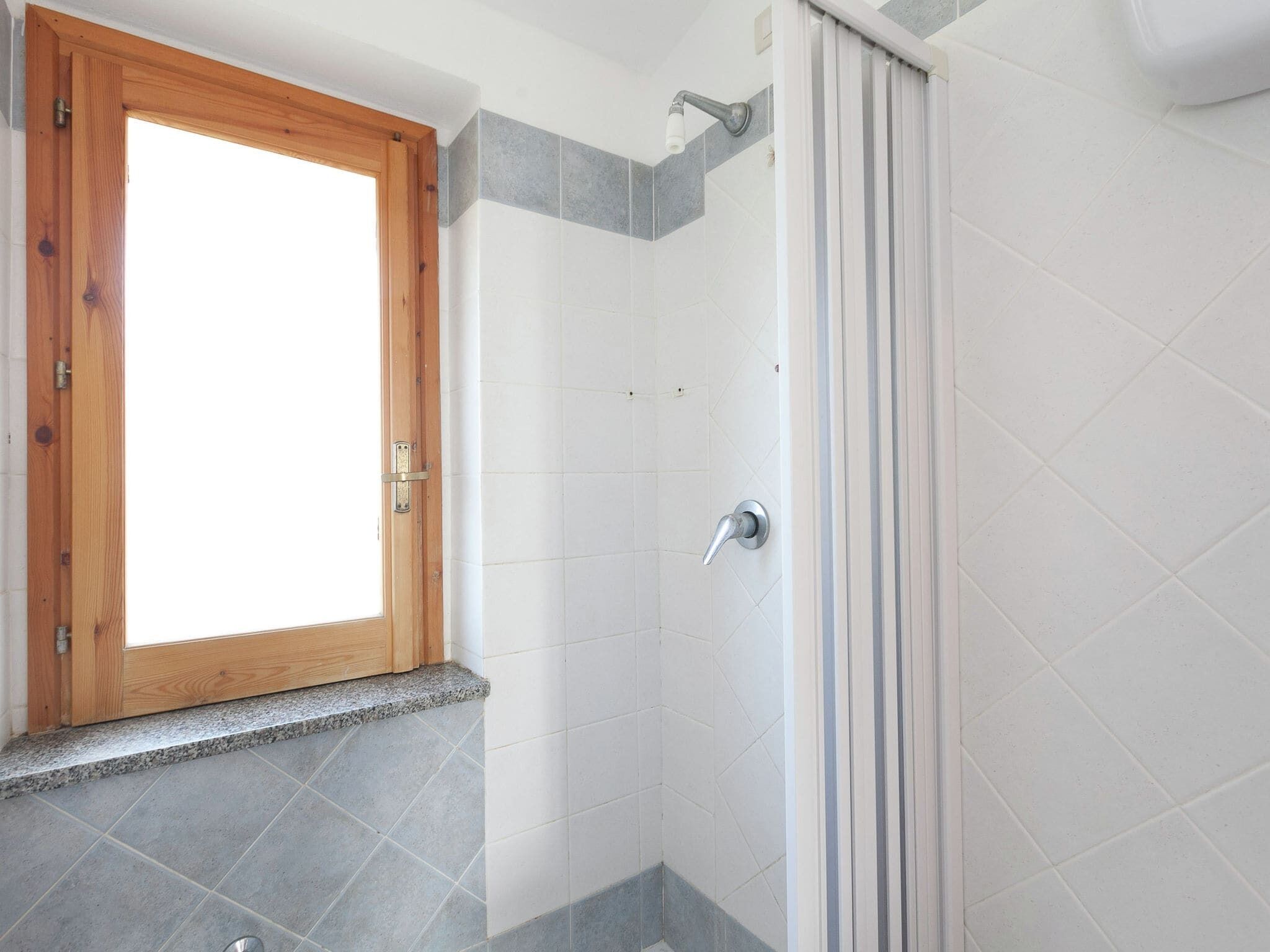 A bathroom with a shower, a wooden door, and a window.