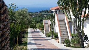 A pathway leading to a building with a red-tiled roof, surrounded by cacti and a view of the sea.