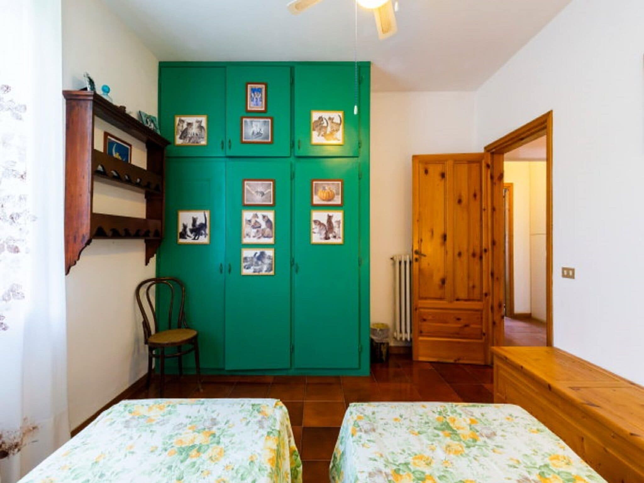 Ein Zimmer mit zwei Betten, einem grünen Kleiderschrank mit Bildern, einem Holzstuhl und einer Holztür.