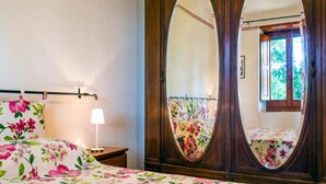 A bedroom with a floral bedspread, a bedside lamp, and a large mirror with a floral curtain.